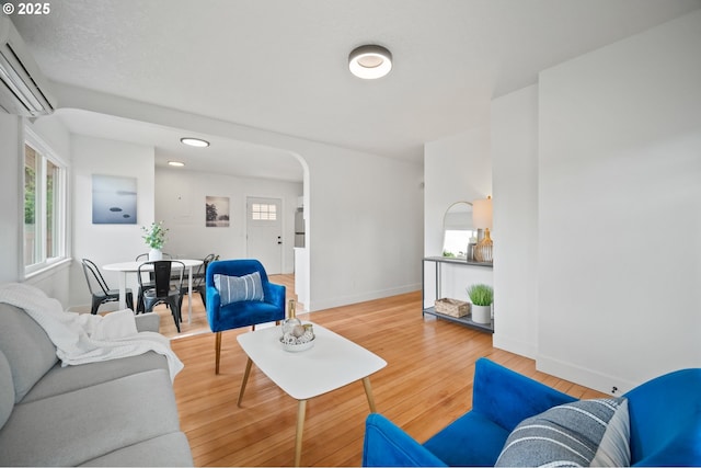 living area with arched walkways, wood finished floors, baseboards, and a wall mounted AC