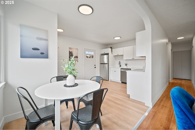 dining space with baseboards, light wood-type flooring, recessed lighting, and arched walkways