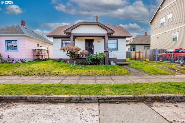 bungalow-style home with a shingled roof, a chimney, a front lawn, and fence