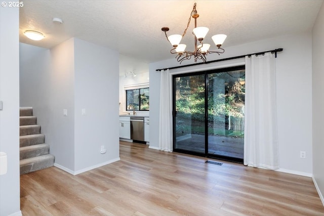 unfurnished dining area featuring a textured ceiling, an inviting chandelier, light hardwood / wood-style flooring, and sink