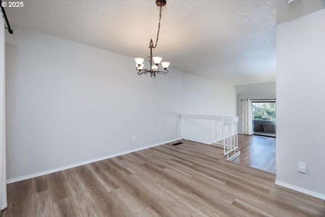 empty room with vaulted ceiling, hardwood / wood-style flooring, a textured ceiling, and a notable chandelier