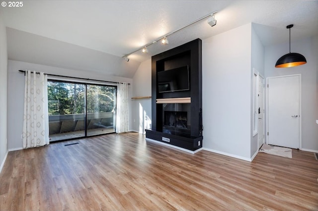 unfurnished living room with a large fireplace, rail lighting, wood-type flooring, and vaulted ceiling