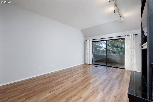 unfurnished room featuring lofted ceiling, track lighting, and light hardwood / wood-style floors