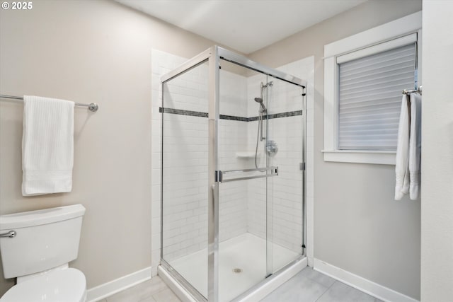 bathroom featuring tile patterned flooring, a shower stall, toilet, and baseboards