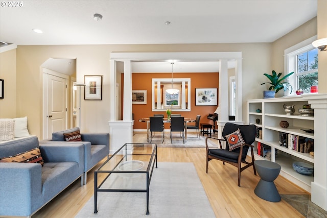 living area featuring light wood-style floors, baseboards, and ornate columns