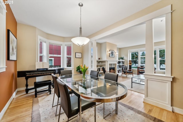 dining space with baseboards, a warm lit fireplace, and light wood-style flooring