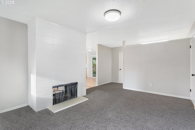 unfurnished living room featuring carpet flooring, a tiled fireplace, and a textured ceiling