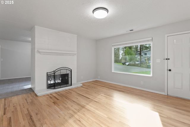 unfurnished living room with a fireplace, light hardwood / wood-style floors, and a textured ceiling