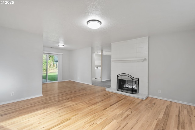 unfurnished living room featuring light hardwood / wood-style floors, a tile fireplace, and a textured ceiling