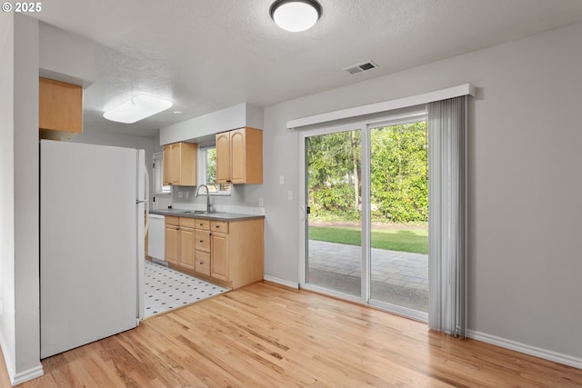 kitchen with sink, white appliances, light hardwood / wood-style floors, a textured ceiling, and light brown cabinets