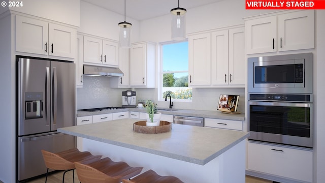 kitchen with appliances with stainless steel finishes, sink, a breakfast bar area, white cabinets, and hanging light fixtures