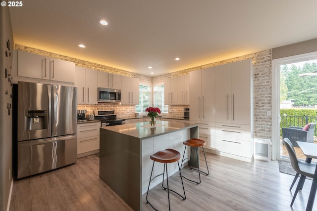 kitchen with a center island, appliances with stainless steel finishes, a kitchen breakfast bar, light hardwood / wood-style flooring, and plenty of natural light