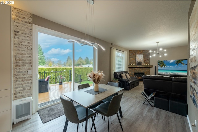 dining room with hardwood / wood-style floors, an inviting chandelier, heating unit, and a stone fireplace