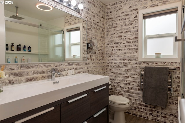 bathroom featuring vanity, hardwood / wood-style flooring, brick wall, and toilet