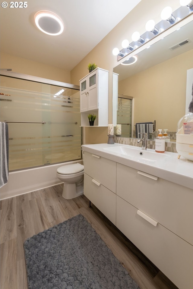 full bathroom with wood-type flooring, toilet, shower / bath combination with glass door, and vanity