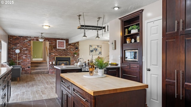 1060 SW 7th St, Hermiston, OR 97838 - kitchen with wooden counters, a kitchen island, open floor plan, brick wall, and a brick fireplace