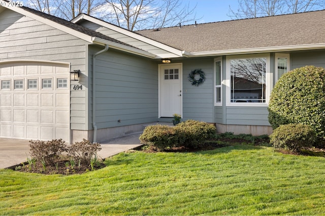 view of exterior entry featuring an attached garage, roof with shingles, and a yard