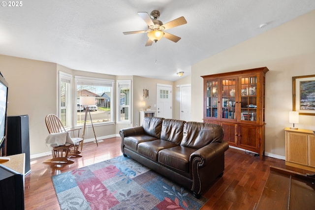 living area featuring ceiling fan, visible vents, baseboards, vaulted ceiling, and dark wood-style floors