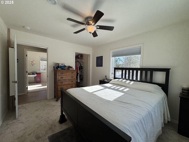 bedroom with ceiling fan, a closet, light carpet, and a walk in closet