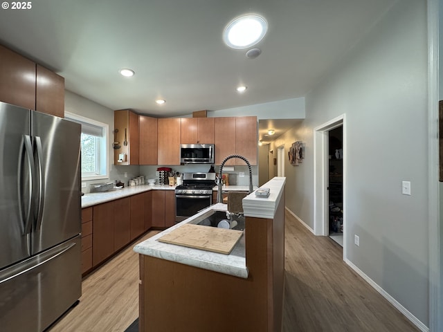 kitchen featuring stainless steel appliances, sink, a kitchen island with sink, and light hardwood / wood-style flooring