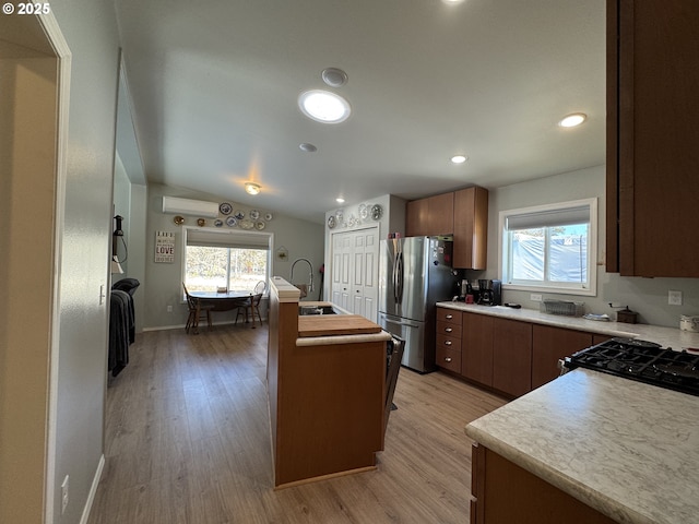 kitchen with stainless steel refrigerator, a healthy amount of sunlight, light hardwood / wood-style floors, and a center island with sink