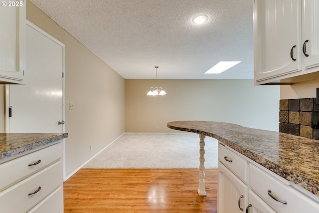 kitchen with decorative light fixtures, white cabinets, a textured ceiling, and light wood-style floors