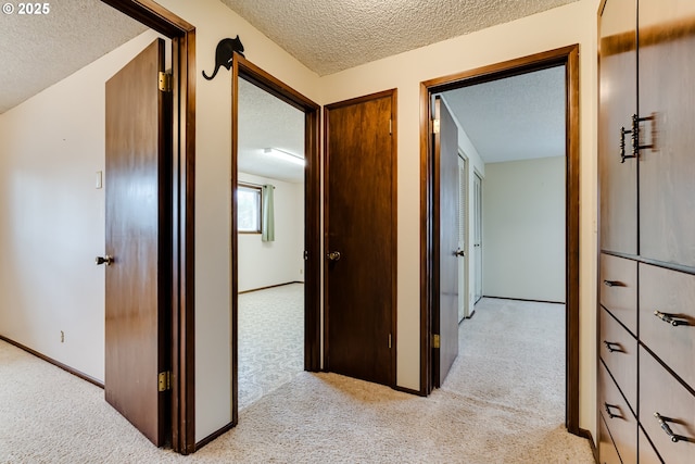 hall with baseboards, light carpet, and a textured ceiling