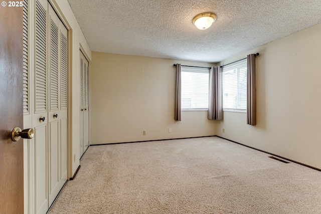 unfurnished bedroom featuring visible vents, baseboards, multiple closets, light colored carpet, and a textured ceiling