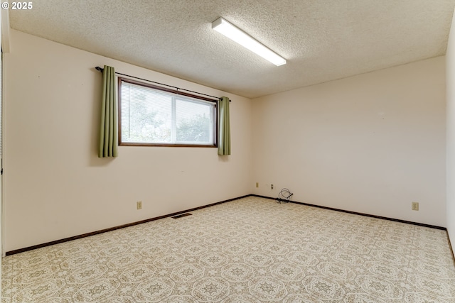 empty room with light colored carpet, baseboards, and a textured ceiling