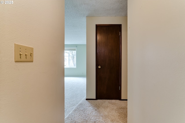 hallway featuring baseboards, a textured ceiling, and carpet