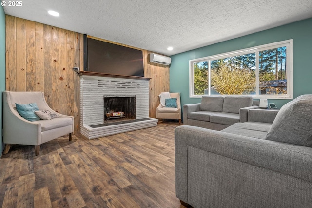 living area with a textured ceiling, a fireplace, a wall unit AC, and wood finished floors