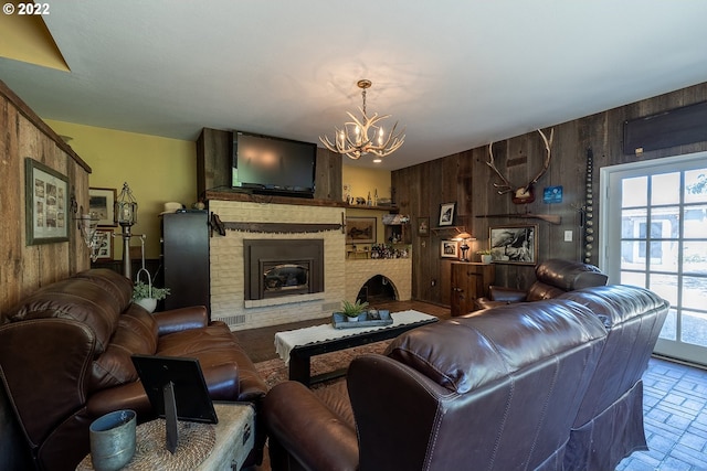 living room with an inviting chandelier, a fireplace, and wooden walls