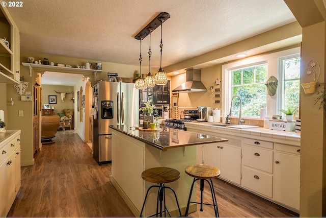 kitchen with range, a center island, stainless steel refrigerator with ice dispenser, white cabinets, and wall chimney exhaust hood