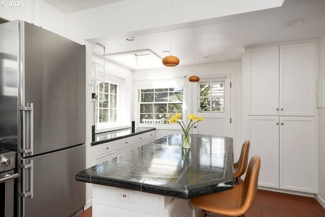 kitchen featuring a breakfast bar, a healthy amount of sunlight, white cabinetry, and high quality fridge