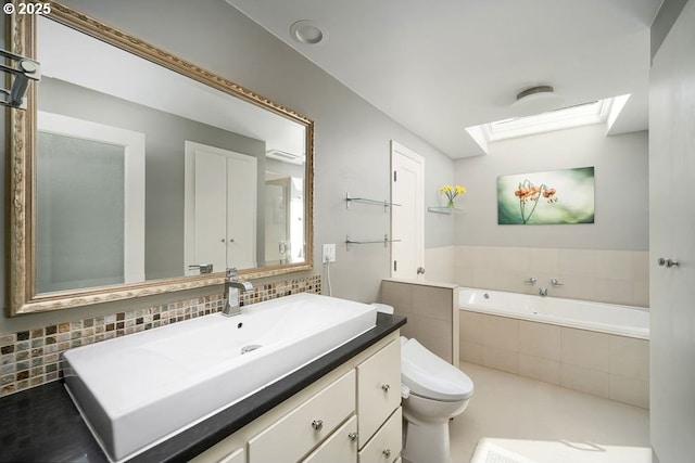 full bathroom featuring tasteful backsplash, toilet, a skylight, a garden tub, and vanity