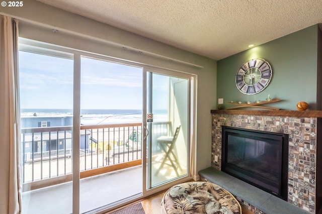 living room with view of water and beach, a textured ceiling, plenty of natural light, a stone fireplace, and wood finished floors