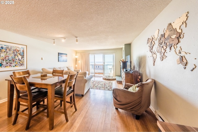 dining area featuring light wood-style floors, a textured ceiling, and a baseboard radiator
