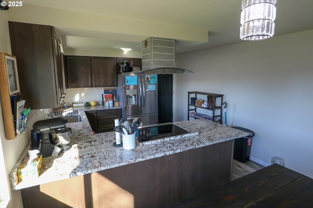 kitchen featuring dark brown cabinetry, stainless steel fridge, island range hood, kitchen peninsula, and light stone counters