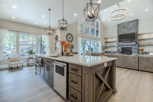 kitchen with sink, a stone fireplace, decorative light fixtures, a center island with sink, and light wood-type flooring