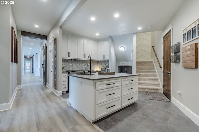 kitchen with a center island with sink, sink, light wood-type flooring, tasteful backsplash, and white cabinetry