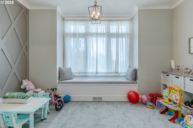 rec room with light wood-type flooring, ornamental molding, and a chandelier