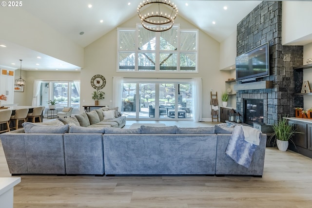 living room with a chandelier, a high ceiling, light hardwood / wood-style flooring, and a stone fireplace