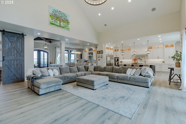 living room with a barn door, french doors, high vaulted ceiling, and light hardwood / wood-style floors