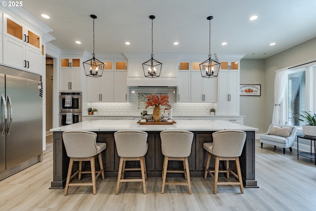 kitchen with white cabinetry, a large island, hanging light fixtures, stainless steel appliances, and light wood-type flooring