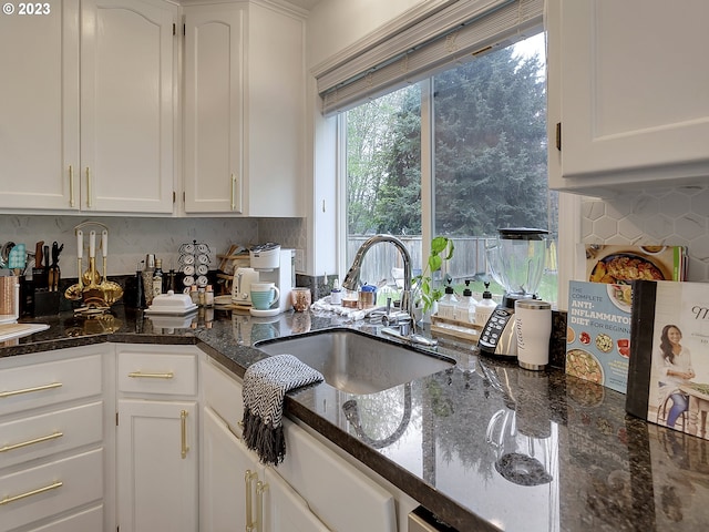 kitchen with white cabinets, dark stone countertops, sink, and tasteful backsplash