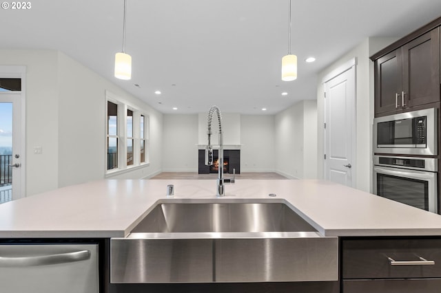 kitchen with dark brown cabinetry, appliances with stainless steel finishes, open floor plan, light countertops, and a sink