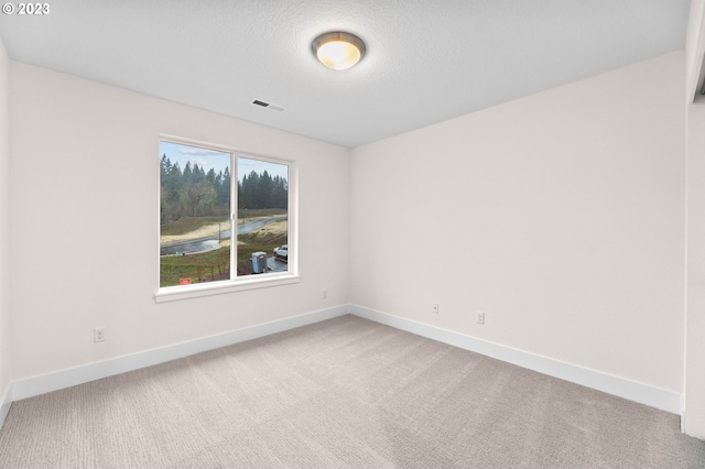 unfurnished room featuring baseboards, a textured ceiling, visible vents, and light colored carpet