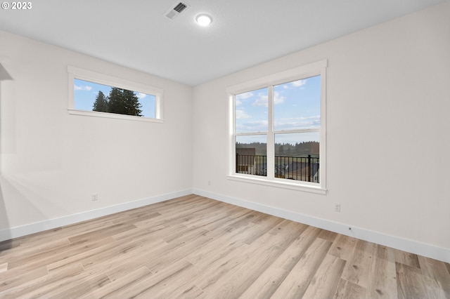 empty room featuring a healthy amount of sunlight, light wood-type flooring, visible vents, and baseboards