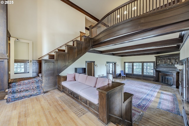 living room featuring crown molding, a towering ceiling, beamed ceiling, and light wood-type flooring