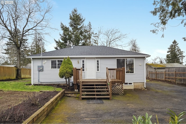 rear view of property featuring roof with shingles, a deck, and fence